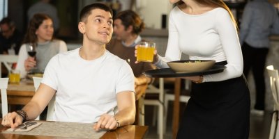 Usmívající se zákazník v restauraci a číšnice, která mu nese nápoj a jídlo