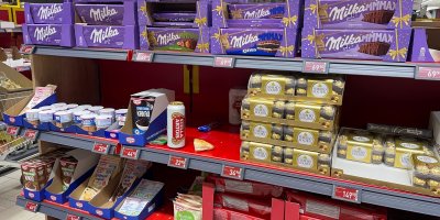 Zbytek rohlíku a plechovka piva mezi zbožím v regálu supermarketu