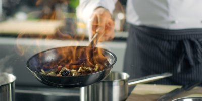 Kuchař smaží na nerezové pánvi, jsou na ní ohnivé plameny