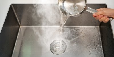 Nalévání horké vody z hrnce do dřezu