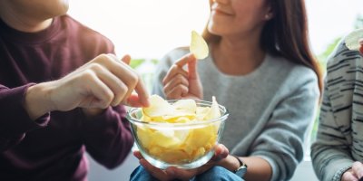 Lidé jedí slané brambůrky ze skleněné mísy.