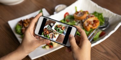 Ženské ruce drží telefon a fotí jídlo na stole