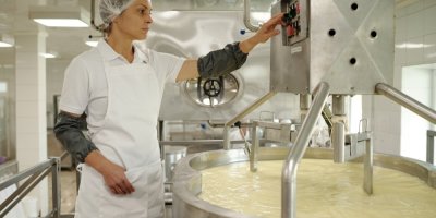 Žena v bílém pracovním oděvu monitoruje průmyslový stroj na výrobu sýrů