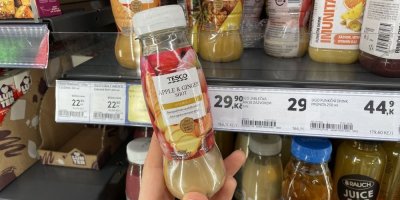 Ruka držící lahev jablečné šťávy se zázvorem v supermarketu