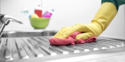 Osoba s gumovými rukavicemi a hadříkem u kuchyňského dřezu