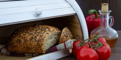 Semínkový chléb na utěrce v chlebníku, vedle jsou rajčata