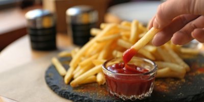 Ruka namáčí hranolku v kečupu
