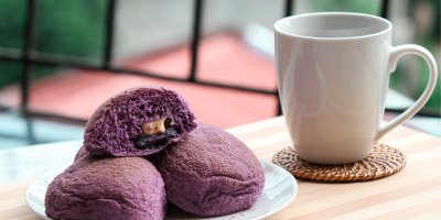 Fialové dezerty na talíři, vedle bílý hrnek