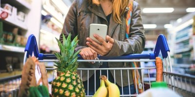 Žena nakupuje v supermarketu a dívá se do telefonu