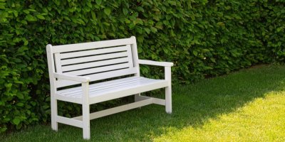 Bílá dřevěná lavička na trávníku před živým plotem