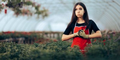 Žena ve skleníku drží lopatku a ve tváři má zmatený výraz.