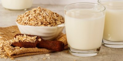 Ovesné vločky v misce a na lžičce, vedle dvě sklenice s mlékem