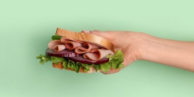 Ženská ruka držící sendvič se šunkou a zeleninou 