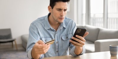 Frustrovaný muž drží v ruce kartu a dívá se do telefonu