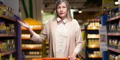 Frustrovaná starší žena s nákupním vozíkem v supermarketu