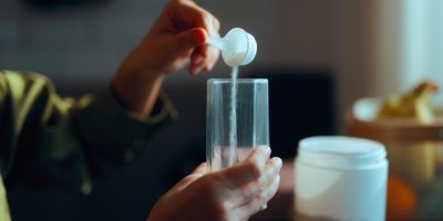 Žena sype práškový doplněk stravy do sklenice s vodou 