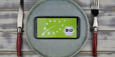 Telefon s logem biopotraviny na prázdném talíři, vedle talíře nůž a vidlička