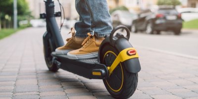 Člověk jedoucí na elektrokoloběžce po městském chodníku