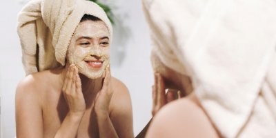 Žena si před zrcadlem aplikuje peeling na obličej