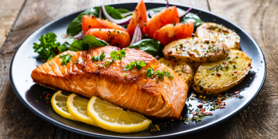 Smažený steak z lososa s bramborami a zeleninou na dřevěném stole