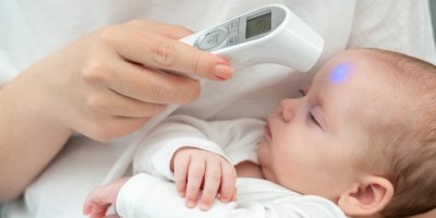 Žena měří teplotu miminka bezkontaktním teploměrem