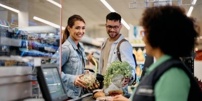 Usmívající se muž se ženou skládají nákup na pás na pokladně.
