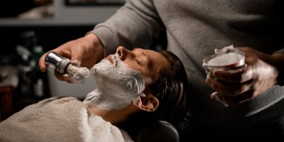 Barber nanáší klientovi na vousy pěnu na holení
