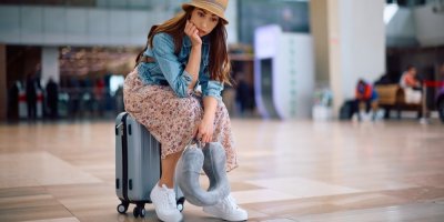 Frustrovaná žena s cestovním kufrem čeká na letišti