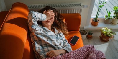 Žena leží na gauči a drží se za hlavu