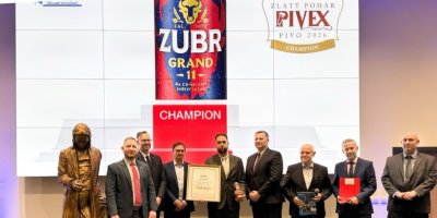 Muži v saku stojí pod displejem s pivem Zubr