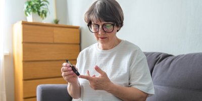 Seniorka si v obývacím pokoji měří hladinu cukru v krvi pomocí glukometru