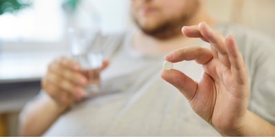 Obézní muž drží v ruce pilulku