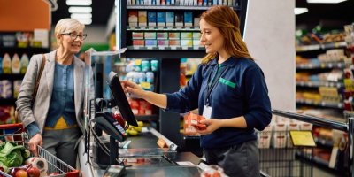 Usmívající se pokladní a starší zákaznice u pokladny supermarketu