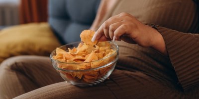 Žena sedí na sedačce s miskou chipsů