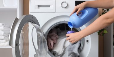 Žena vedle pračky nalévá prací gel do odměrky 