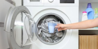 Ženská ruka držící prací prostředek před pračkou plnou prádla