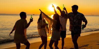 Skupina veselých přátel pije alkohol na pláži při západu slunce