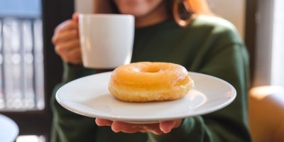 Žena s donutem na talíři a hrnkem kávy
