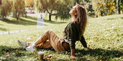 Mladá žena sedí na trávníku v parku a relaxuje