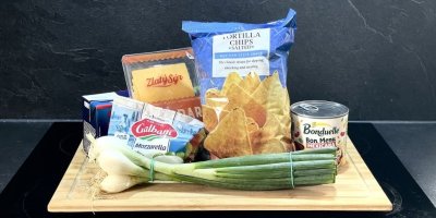 Tortilla chips, mozzarella, cheddar, jarní cibulka, rajčatový protlak a fazole v konzervě na dřevěném prkénku