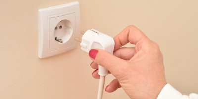 Ženská ruka držící bílý elektrický kabel vedle bílé elektrické zásuvky
