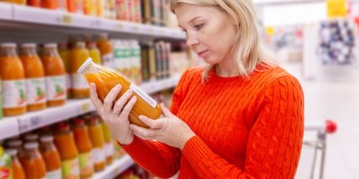 Žena si čte etiketu na skleněné lahvi ovocného nápoje v supermarketu