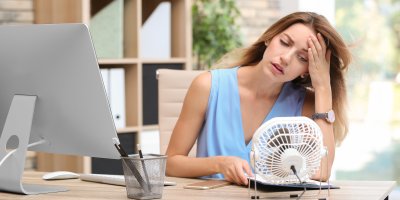 Žena se u stolu chladí o přenosný ventilátor
