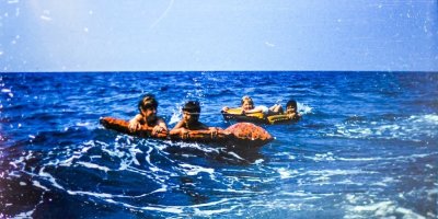 Stará fotografie ženy a dětí s nafukovacími lehátky v moři