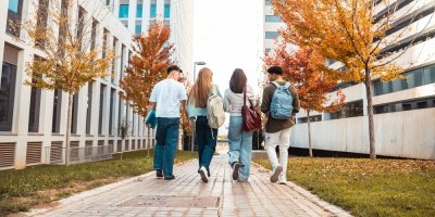 Čtyři studenti kráčí po chodníku podél budovy školy