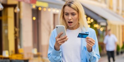 Šokovaná mladá žena s platební kartou a mobilním telefonem