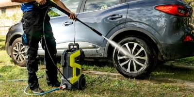Muž v pracovním oděvu umývá auto vysokotlakým čističem