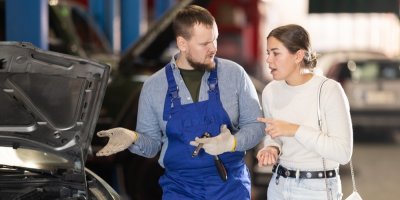 Automechanik mluví s mladou zákaznicí v autoservisu