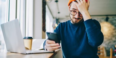 Muž sedící v kavárně se dívá do telefonu a chytá se za hlavu