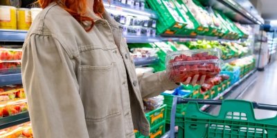 Žena v supermarketu drží plastové vaničky s čerstvými malinami 